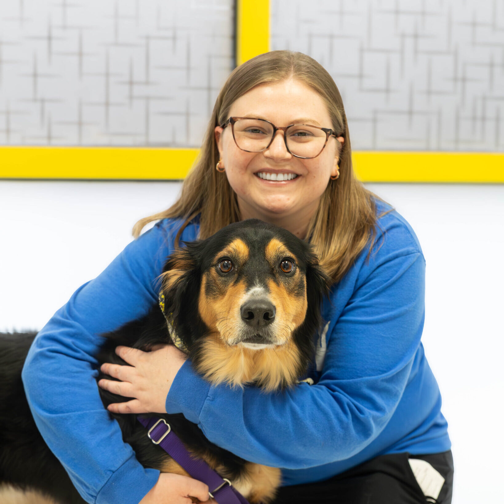 woman with glasses smiling and hugging a brown and black dog